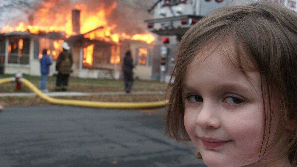 A girl smiling while standing in front of a burning house