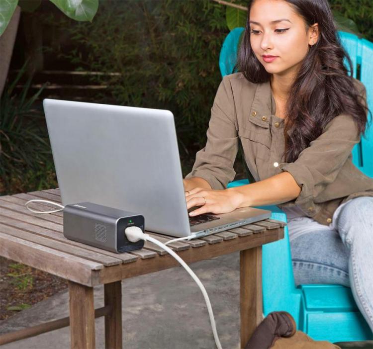 A girl is sitting on a sky blue colored chair on a ground while working on a laptop which is placed on a wooden table