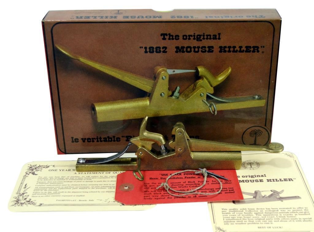 A golden colored metal 1862 Mouse Trap on a piece of paper and one golden colored metal 1862 Mouse Trap on a wooden ox