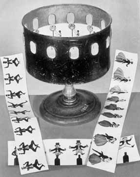 Black and white pic of a black colored dancing man painted on white paper and a black colored circular lamp-like zoetrope apparatus on a grey table