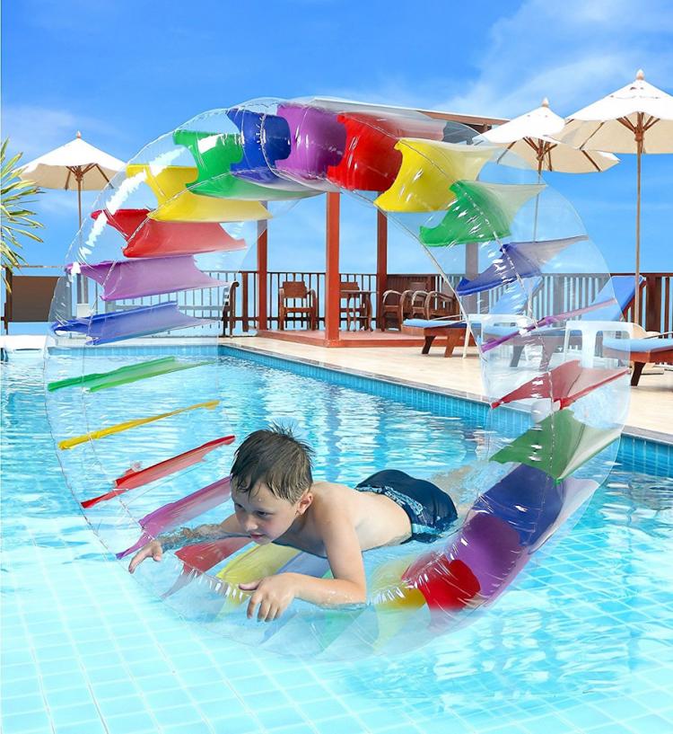 A oy lying in a transparent wheel with multi-colored layers inside it in a swimming pool