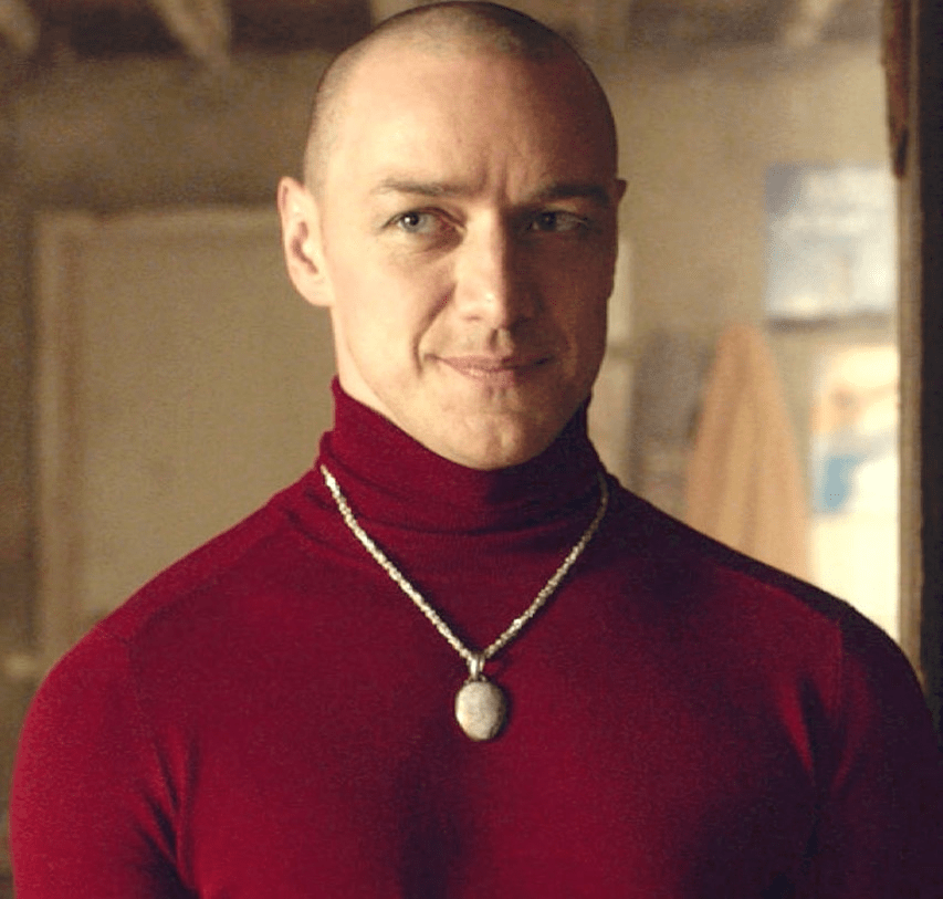A bald man wearing a red turtle neck and a necklace