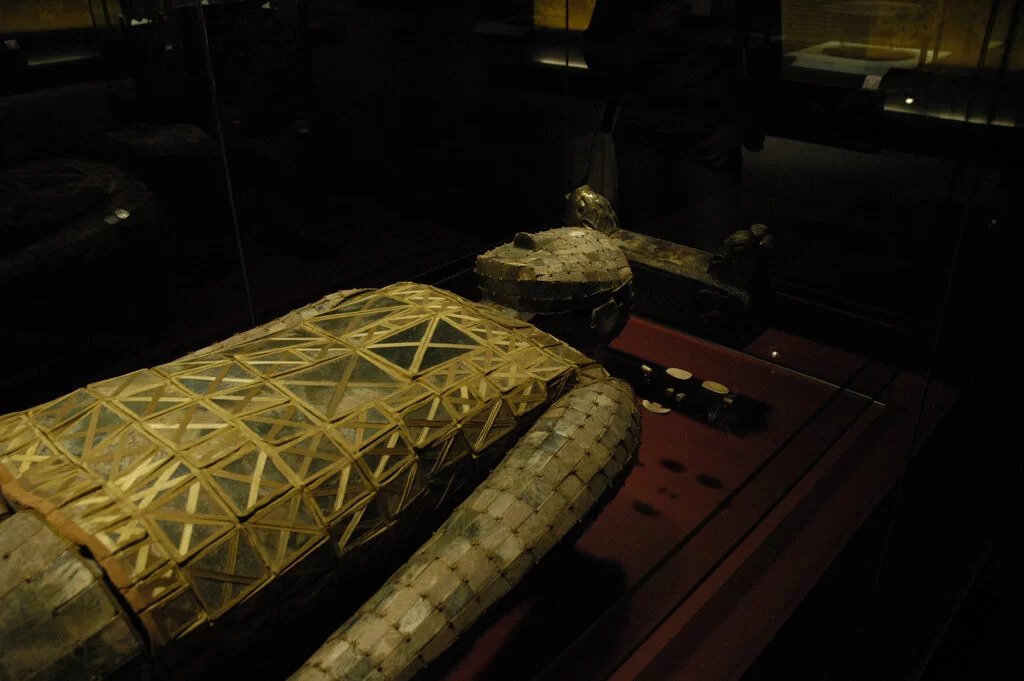 An angular view of metal and jade burial suit on a brown wooden surface