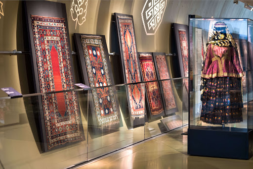 Multicolored carpets and a female dress displayed at carpet museum in Baku