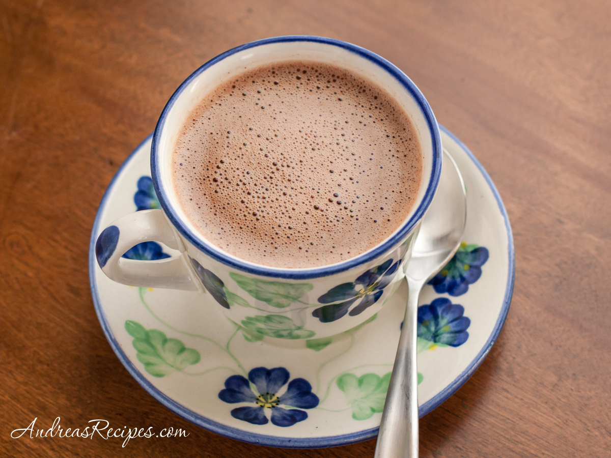 A cup of hot chocolate in a saucer with a teaspoon beside the cup