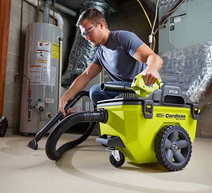 Green and black colored cleaner, operated by a grey shirt and jeans wearing man, on a concrete floor