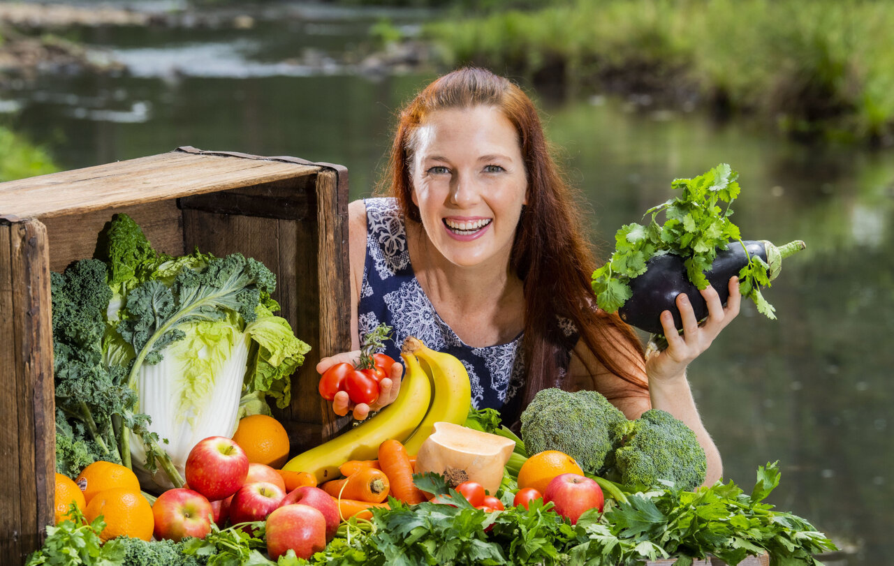 A woman smiling while holding an eggplant and with some vegetables 