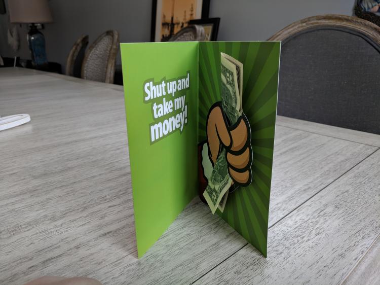 Green colored Take My Money Pop Up Birthday Card on a white-grey wooden table