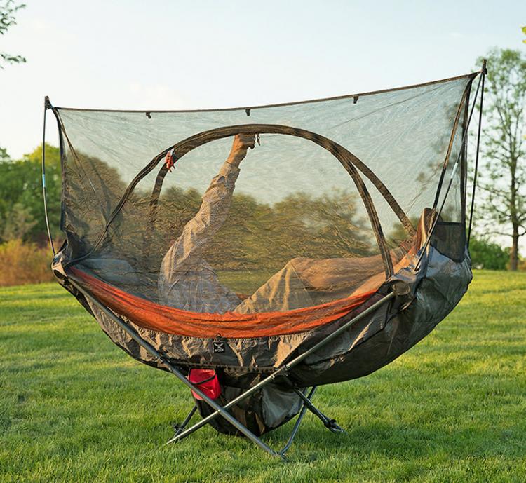 A man resting on the foldable chair hammock in the grassy land