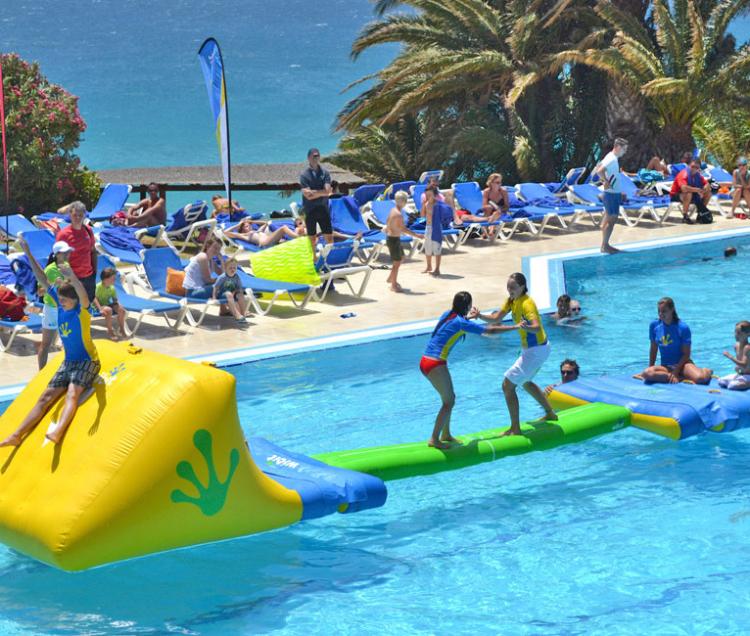 People playing on yellow, blue and green pool toy set in a swimming pool