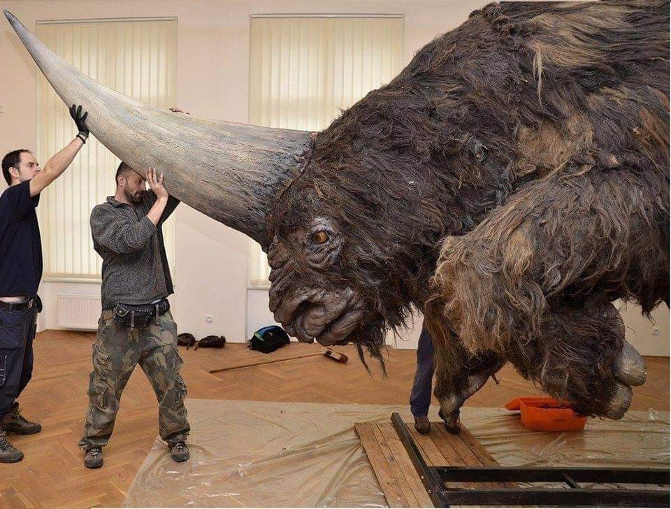 Two men holding the horn of life-size realistic sculpture of Elasmotherium