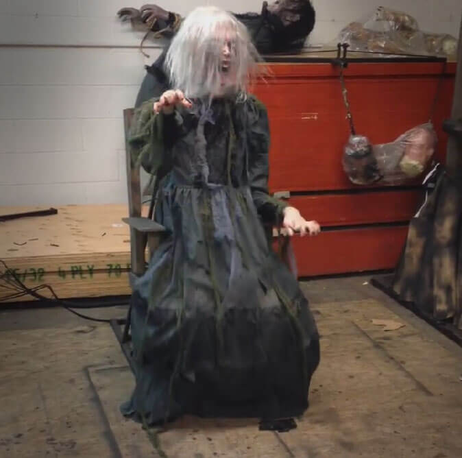 Spooky old lady sitting on a chair in an abandoned area wearing long black gown