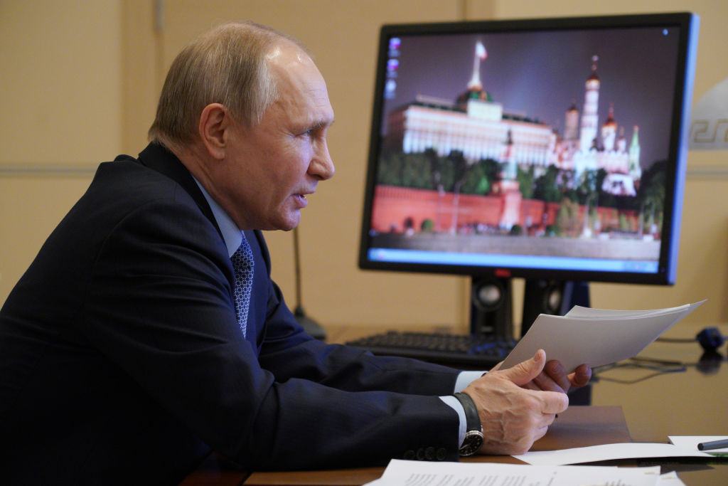 At his office, President Putin holds documents and beside him a monitor showing beautiful building structure