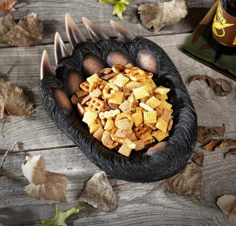 A black colored serving bowl filled with snacks surrounded by leaves on a wooden table