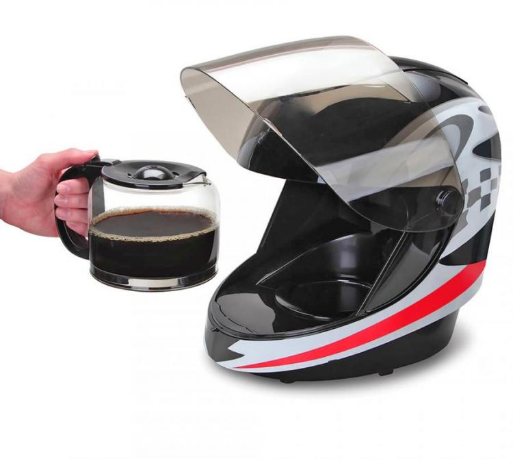 A motorcycle helmet coffee maker with a grey, black and red pattern, a hand holding a black coffee jar