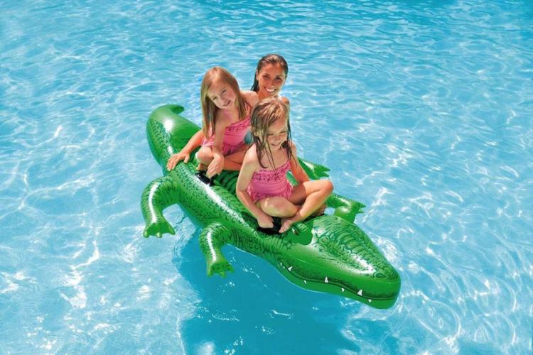 Three girls sitting on a green alligator shaped float in a swimming pool
