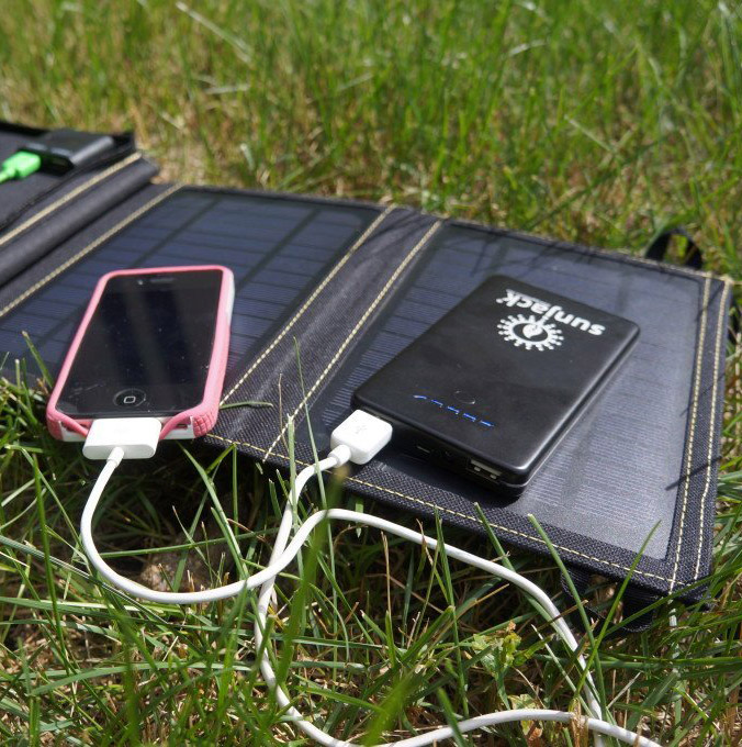 Slim and smart black colored solar charger on a ground, charging a phone and another device