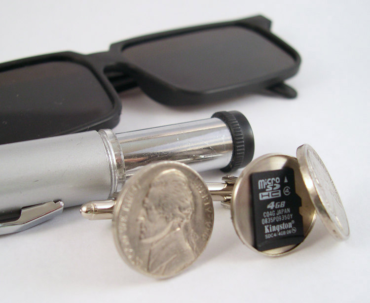 A secret compartment coin cufflink with black glasses and silver pen on white surface