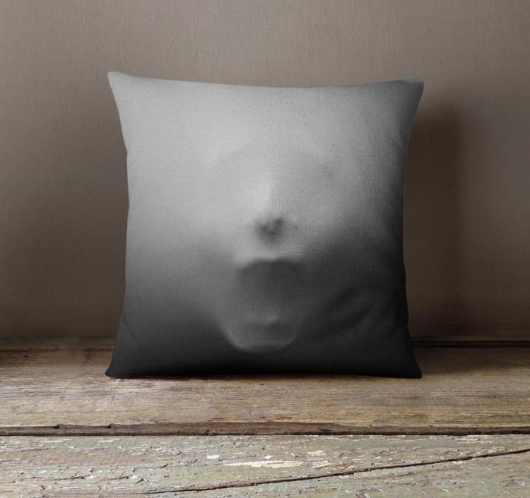 Grey colored pillowcase, with a 3d face printed on it, on a wooden table