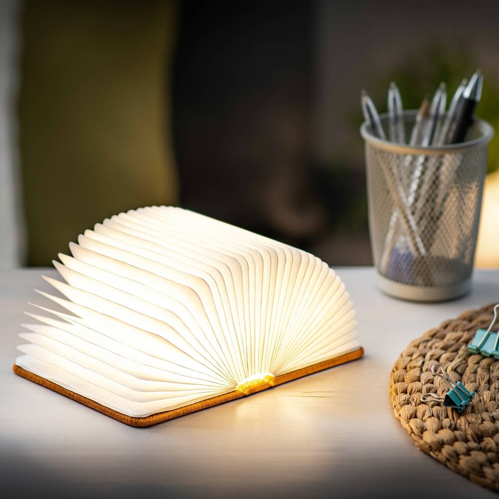 An opened book lamp beside a pen holder and a table cloth on a white table top