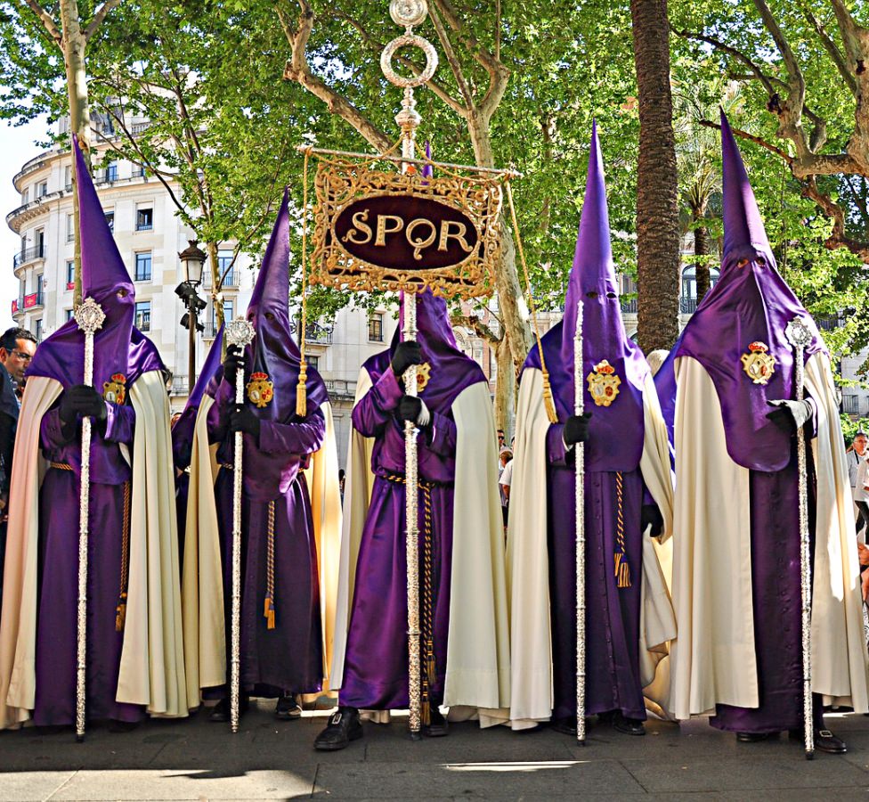 A group of people wearing purple and white cloaks and holding long silver sticks