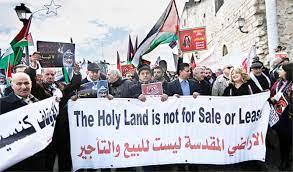 Palestinians holding flags and banners that says 'The Holy Land is not for Sale or Lease'