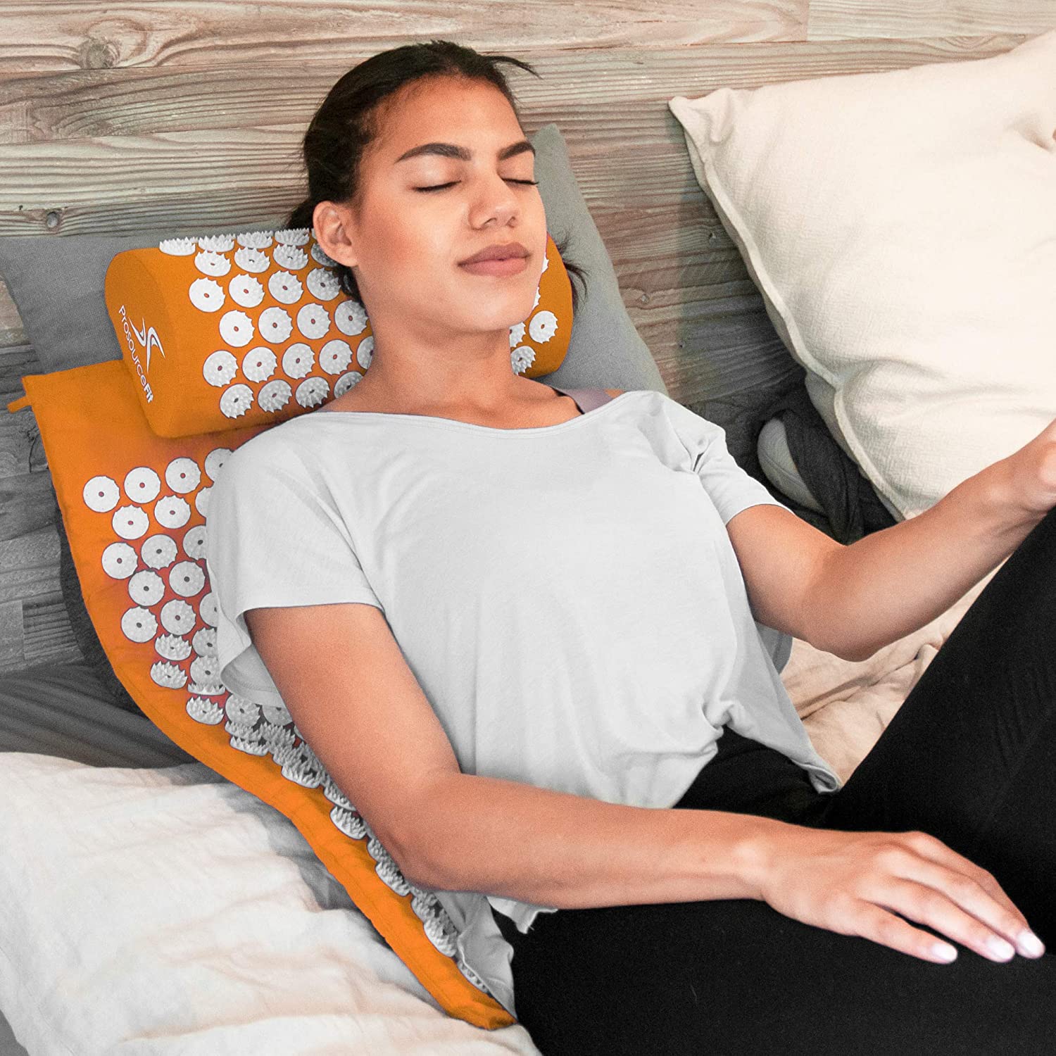 A woman resting on an orange Acupuncture Mat And Pillow on a bed