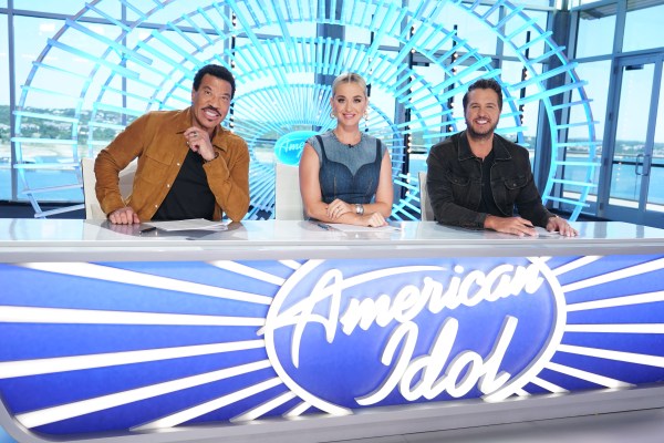 Three American idol judges are sitting and smiling at the camera