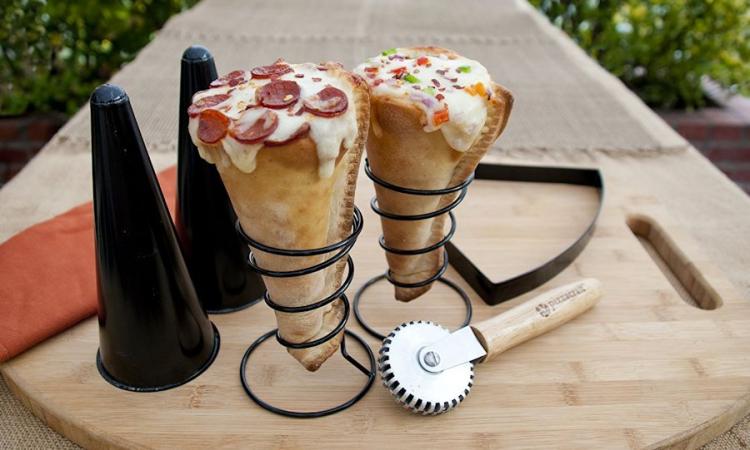 Grilled pizza cone in a cone stand with cone mold and a pizza cutter on a wooden board