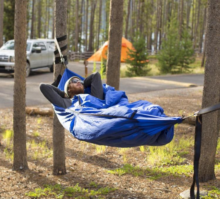 A man resting on a blue sleeping bag hammock in front of the road