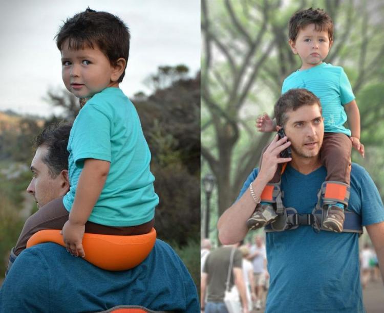 A man carrying a light blue shirt wearing kid on his shoulders with the help of an orange saddlebag