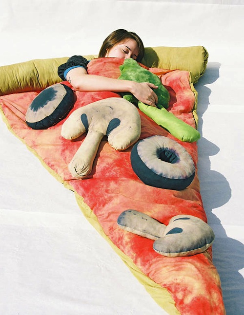 A girl sleeping in a pizza-themed bed with mushrooms, olives and vegetables cushions