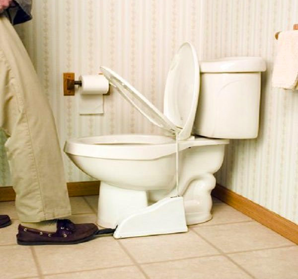 A man wearing skin-colored pants and dark brown shoes pushing the white pedal of a white commode