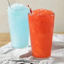 Red and light blue colored slush in glasses with straws placed on a grey cloth