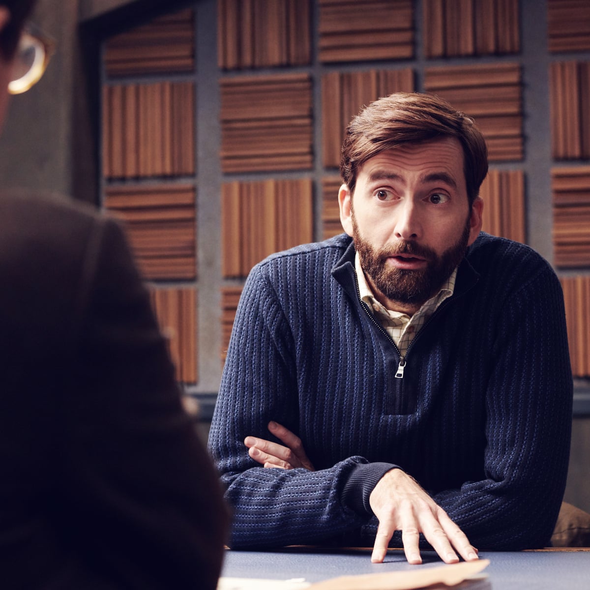 A bearded man wearing a blue sweater sitting at the table 