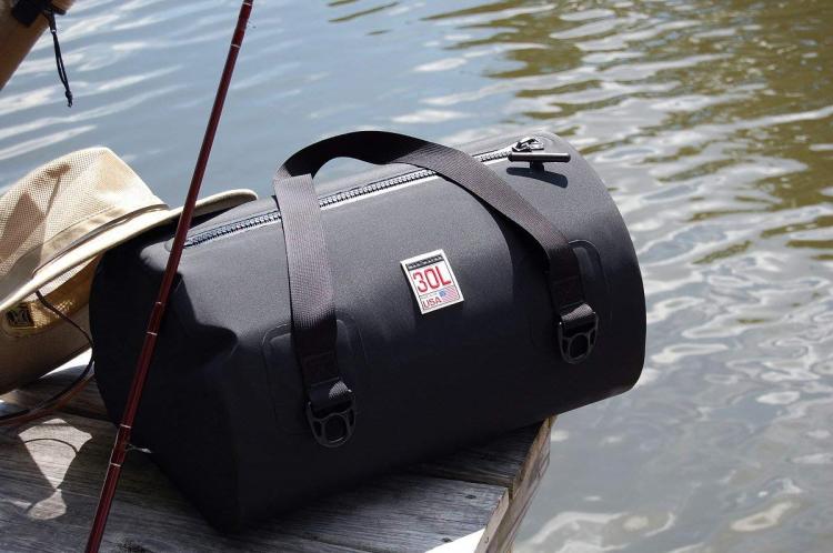 Black colored waterproof bag with a fishing rod, cap and fishing rod in front of alake 