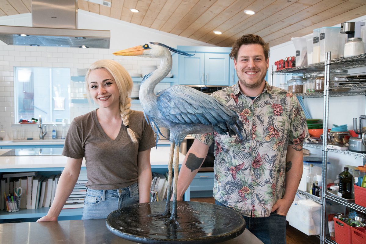 Natalie sideserf and his husband standing next to a hyper-realistic blue and white-colored bird cake