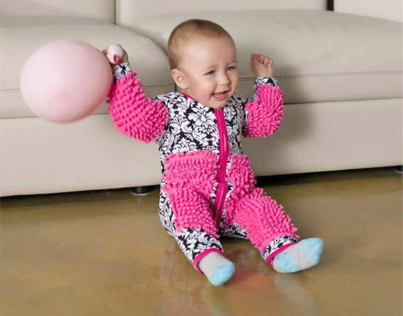 In front of the couch is a baby wearing onesie pink baby mop dress