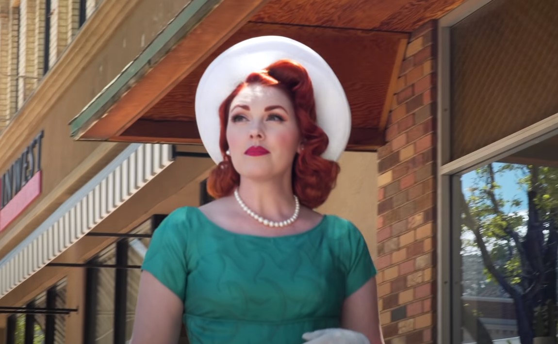 Luci Fay wearing a aqua green colored vintage dress and a white colored hat walking in the streets