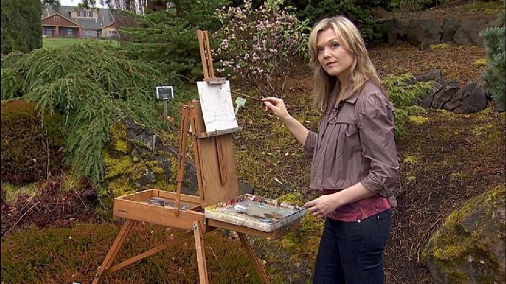 Ariana Richards stares at the camera while holding a paintbrush outside her house
