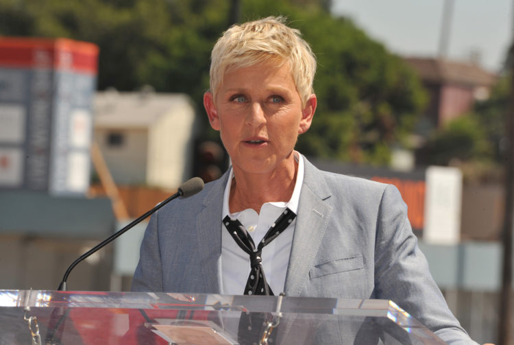 Ellen DeGeneres wearing a suit and a tie speaking through a mic