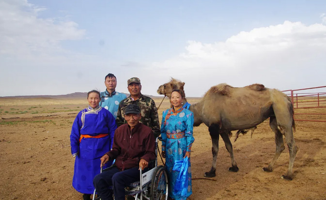 A camel is standing with its owners in a desert