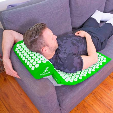 A man wearing a black shirt sleeping on a green Acupuncture Mat And Pillow on a grey sofa