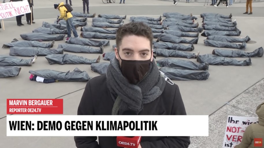 A male reporter wearing a black-colored facemask and behind him are the corpse