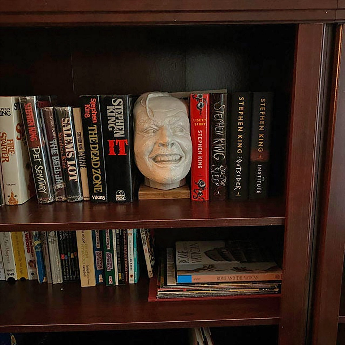 White ceramic 'The Shining' Bookend between a tuft of books on a dark brown wooden bookshelf
