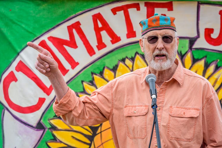 James Cromwell wearing a colorful bonnet while his right hand is pointing somewhere