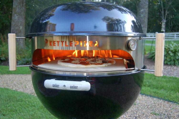 A giant black colored oven grilling pizza in backyard