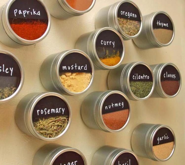 Stainless steel metal spice magnetic jars on a skin wall which includes rosemary, nutmeg, garlic, cilantro, curry, paprika, etc.