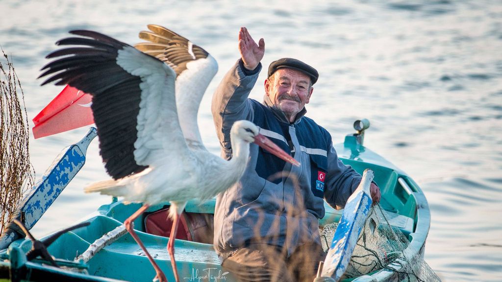 A fisherman waving his hand and stork yaren flapping its wings