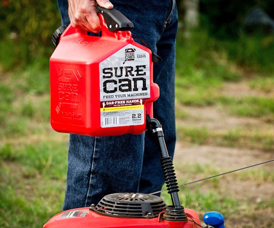 A blue jeans-wearing man filling gas in a lawn mower with the red colored sure can in the garden